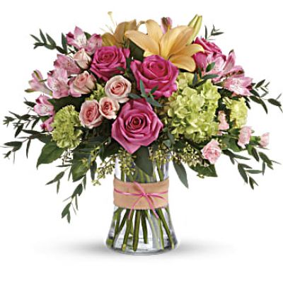 Put a spring in their step with this beautifully blushing bouquet of hot pink roses, soft peach lilies and fresh green hydrangea. Arranged in a graceful vase tied with a charming bow, it's a chic treat for any occasion!
